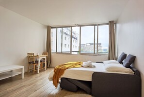 Habitación de hotel con cama, escritorio y silla. Ventana con cortinas y vista de edificios.