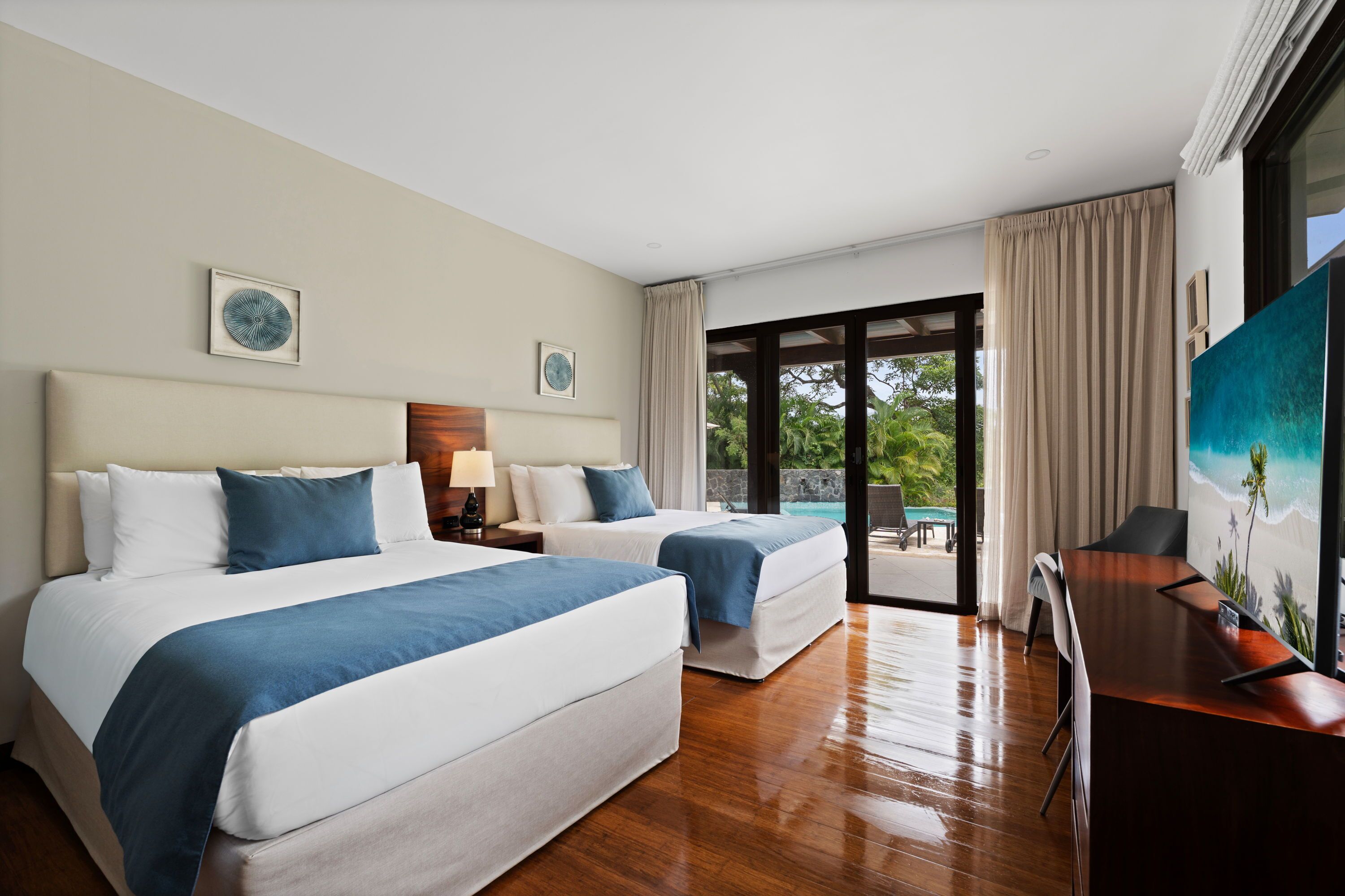 A hotel room with two beds, a desk, and a view of the outdoors.