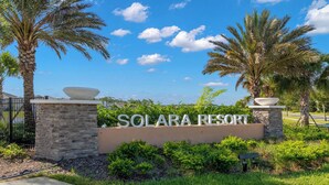 A sign for Solara Resort with a clear sky and palm trees.