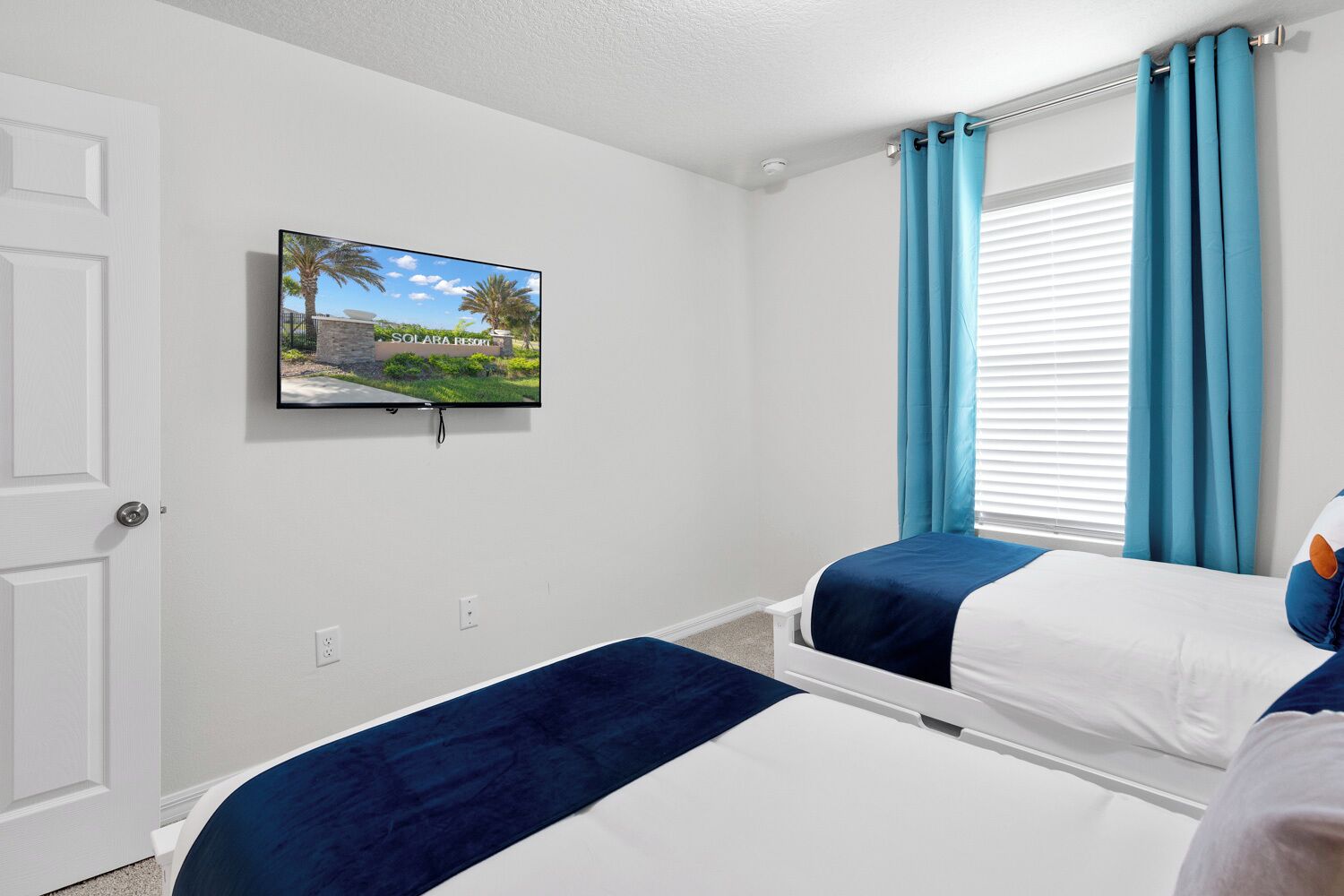 A hotel room with two beds, a TV on the wall, and a window with curtains.