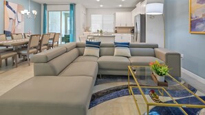 A modern living room with a sectional sofa, a dining table, and a kitchen in the background.