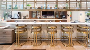 A modern kitchen with a bar area, featuring stainless steel appliances, a large flat-screen TV, and a wooden bar counter with stools.