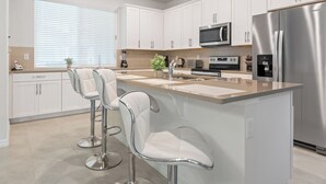 A modern kitchen with white cabinets, stainless steel appliances, and a central island with bar stools.
