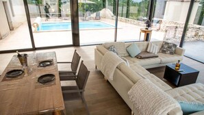 A modern living room with a dining table, sofa, and a view of a swimming pool. - Le Rocal, close to Monbazillac in the shadow of Bergerac (Pomport)