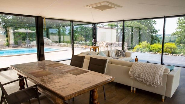 A modern living room with a dining table, sofa, and large windows overlooking a pool and garden. - Le Rocal, close to Monbazillac in the shadow of Bergerac (Pomport)