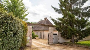 A rustic house with a gravel driveway leading to a gated entrance, surrounded by greenery and a large evergreen tree. - Le Rocal, close to Monbazillac in the shadow of Bergerac (Pomport)