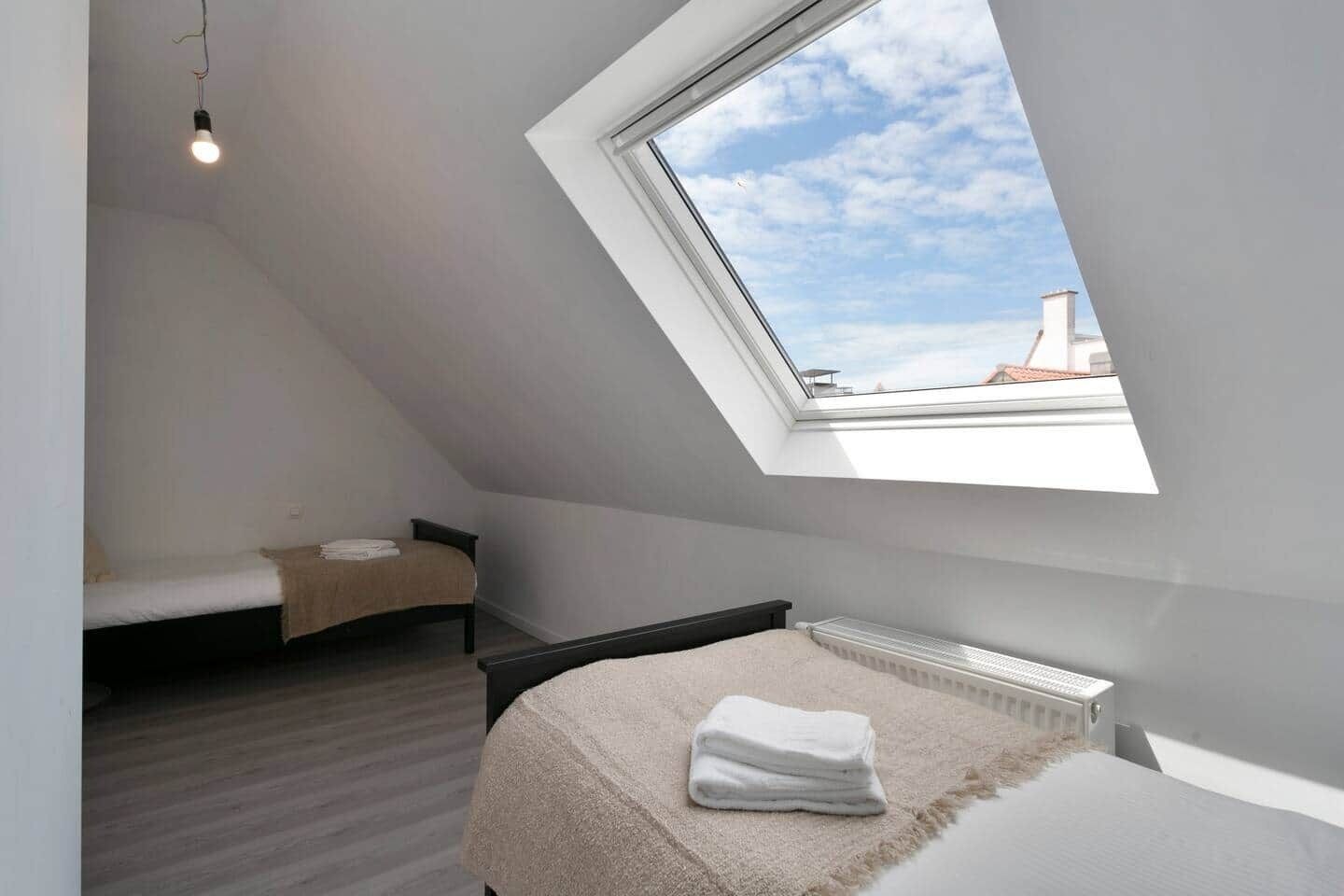 A small, modern bedroom with a skylight, a bed, a bedside table, and a radiator.