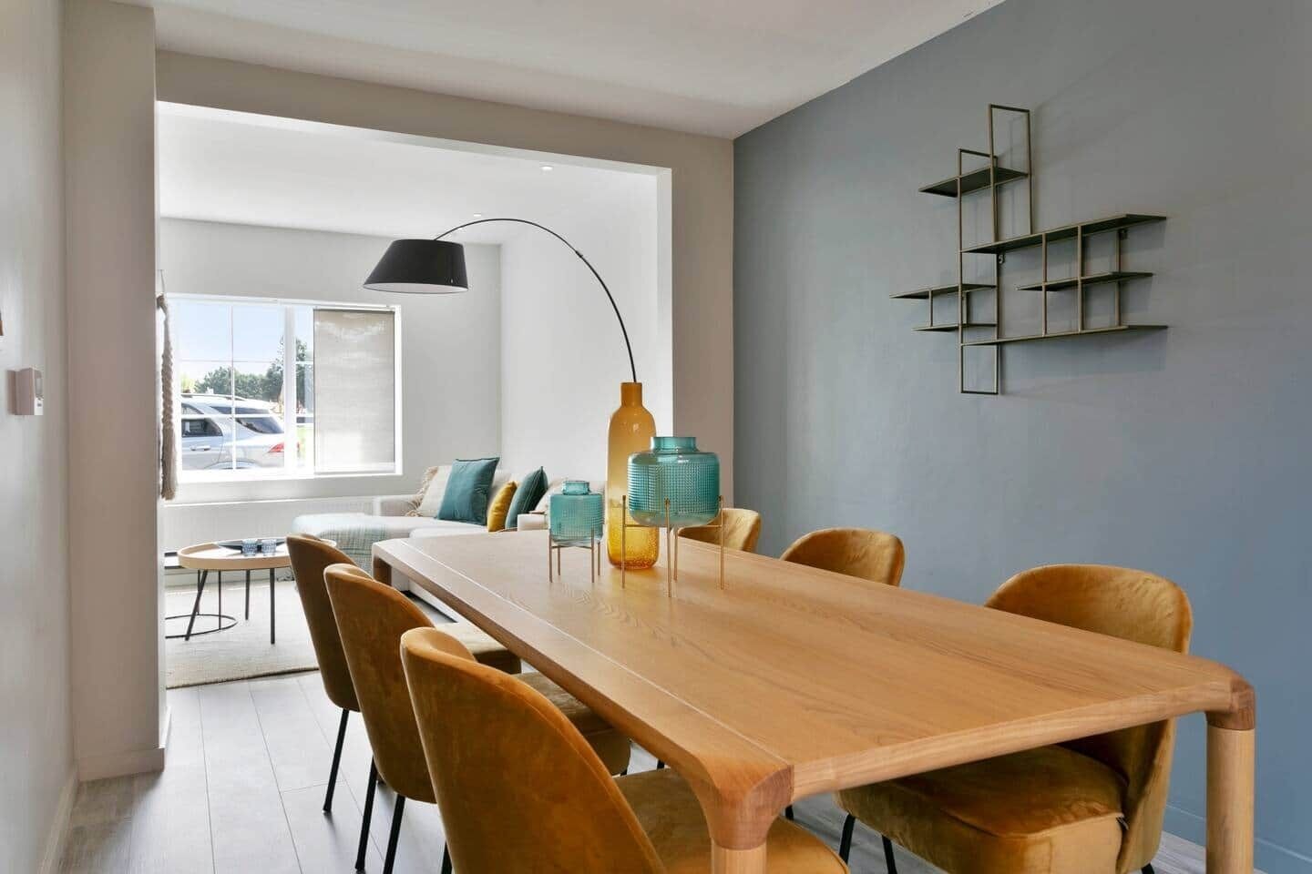 A modern dining area with a wooden table and chairs, a pendant lamp, and a wall-mounted shelf unit.