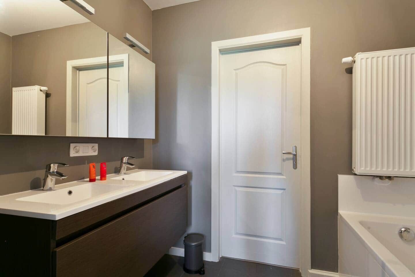 A bathroom with two sinks, a mirror, a door, and a radiator.