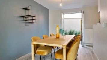 A dining area with a wooden table and velvet chairs, a pendant light, and a view through a large window.
