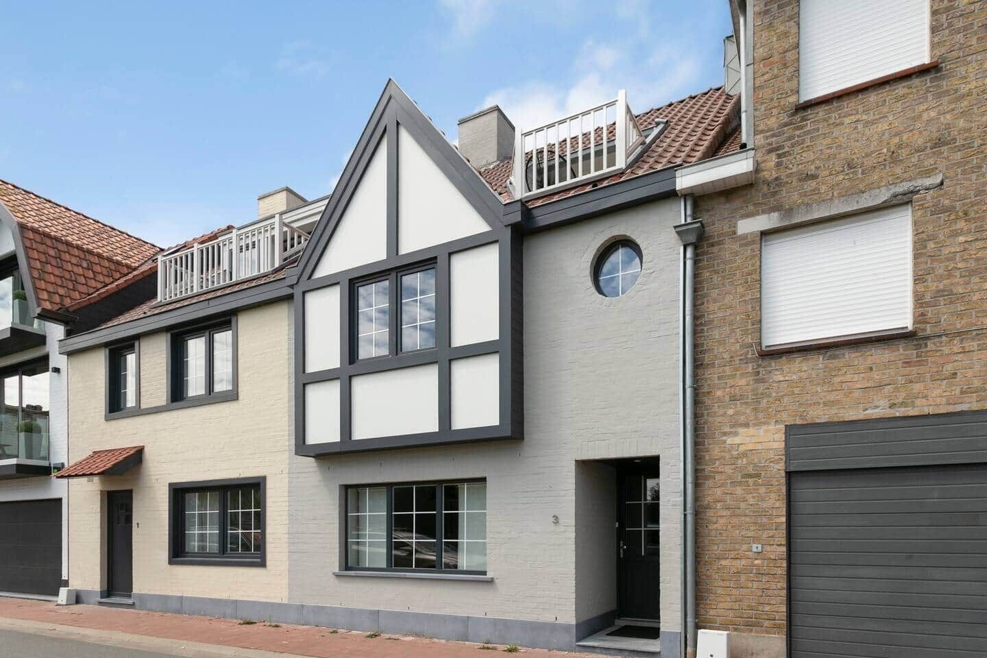 Een woonhuis met twee verdiepingen, een puntdak, dakkapellen en een balkon.