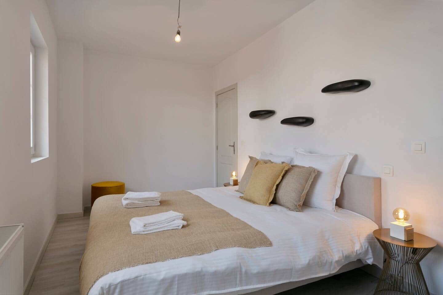 Een slaapkamer met een bed, kussens, een nachtkastje en een lamp.