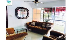 A living room with a brown sofa, two armchairs, a glass coffee table, and a decorative mirror on the wall.