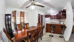 A dining area with a wooden table and chairs, a bar with stools, and a ceiling fan.