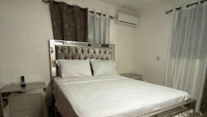 A bedroom with a bed, a nightstand, an air conditioning unit, and a ceiling fan.