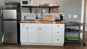 A compact kitchen with a refrigerator, microwave, and a small sink. There is a wooden countertop, a shelf with dishes, and a small cart with pots and pans. - Lake Front Rental in Panama City with Kayak, EV Charger, & Dock - Dog Friendly (Southport)