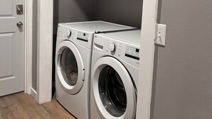 A laundry room with two front-loading washing machines, a fire extinguisher on a shelf above, and a door to the left. - Lake Front Rental in Panama City with Kayak, EV Charger, & Dock - Dog Friendly (Southport)