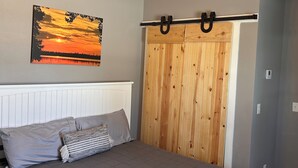 A bedroom with a bed, a ceiling fan, a wooden wardrobe, and a sunset painting on the wall. - Lake Front Rental in Panama City with Kayak, EV Charger, & Dock - Dog Friendly (Southport)
