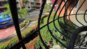 A view through a metal gate of a street with parked cars and buildings in the background. - Santo Domingo huge furnished longterm available apt (Santo Domingo norte)