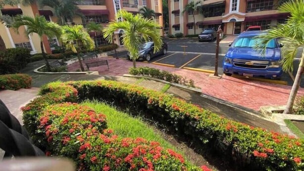 A multi-story hotel with a central courtyard, palm trees, and a parking area with cars. - Santo Domingo huge furnished longterm available apt (Santo Domingo norte)