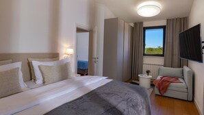 A hotel room with a large bed, a seating area with a chair, a small table, and a TV mounted on the wall. - Charming Casa Piccola - 5 minutes' walk to the nearest beach! (Umag)