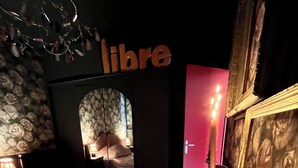 A dimly lit bedroom with a bed, a vanity with a mirror, a wall with a 'libre' sign, and a candle on a tray. - Bohemian boudoir-style artist apartment. (Royan)