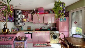A kitchen with pink cabinets, a washing machine, a microwave, and a dining area with a table and chairs. - Bohemian boudoir-style artist apartment. (Royan)