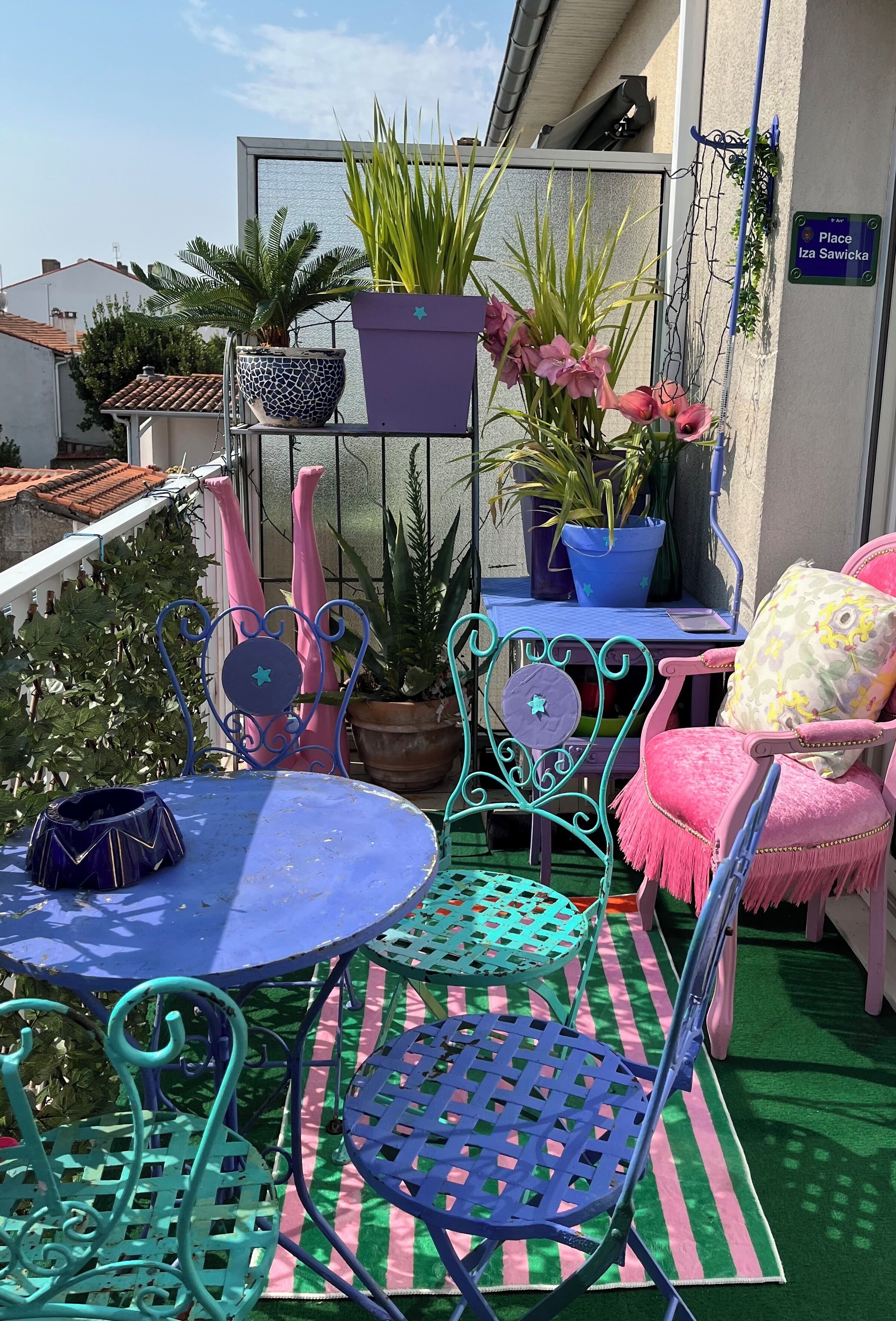 Uma varanda com mesa azul, cadeiras verde-água e plantas em vasos.