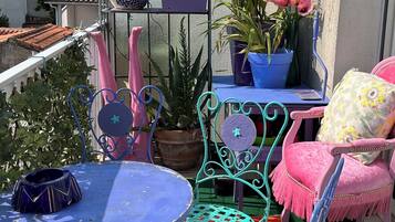 Uma varanda com mesa azul, cadeiras verde-água e plantas em vasos.