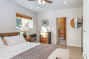 A bedroom with a bed, a dresser, a radiator, a window with blinds, a ceiling fan, and a door leading to another room.