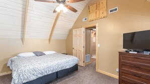 A bedroom with a bed, a ceiling fan, a dresser, and a television.
