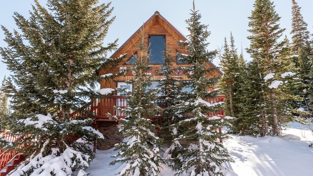 Eine Holzhütte, umgeben von schneebedeckten Bäumen und einer Holzterrasse.