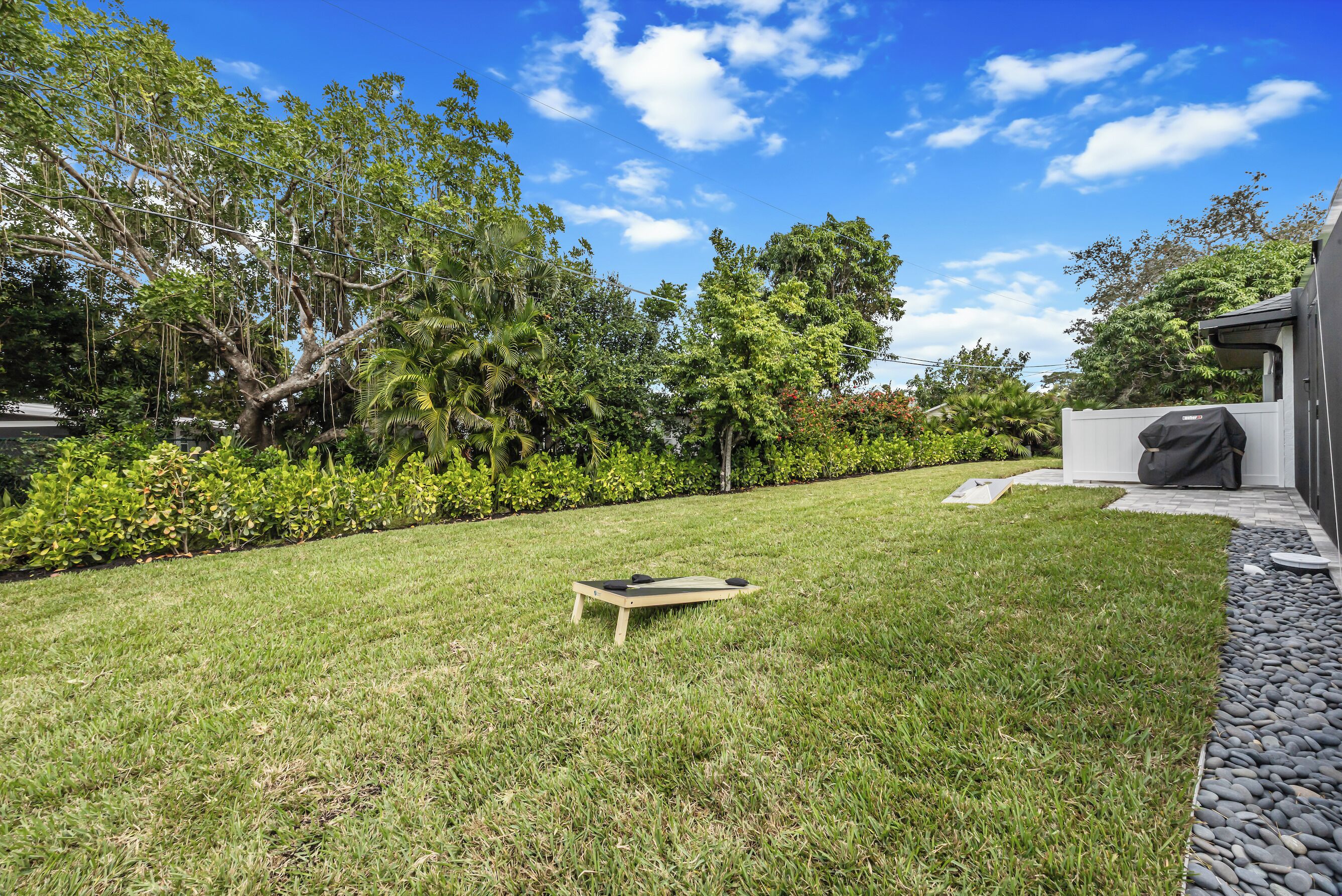 Un jardin bien entretenu, avec une terrasse en bois, un barbecue et une variété d’arbres et d’arbustes.