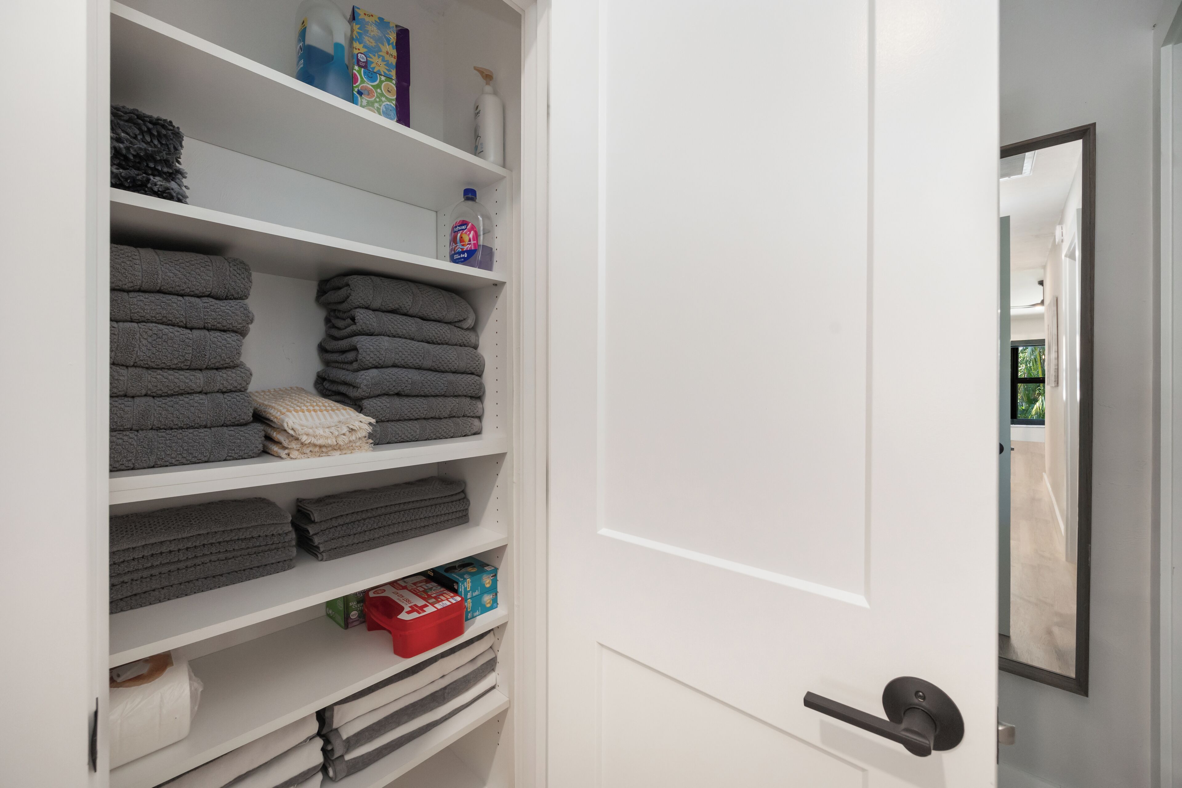 Een witte kast met planken vol opgevouwen handdoeken en toiletartikelen.