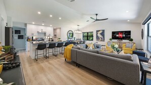A modern kitchen with bar stools, a grey sofa, and a yellow throw blanket.
