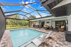 A pool area with a glass ceiling, outdoor furniture, and a view of the surrounding greenery.