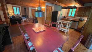 Un vaste espace dédié à la salle à manger, avec une table et des chaises en bois, un luminaire suspendu et une cuisine en arrière-plan.