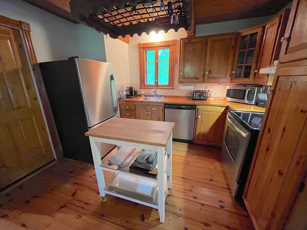 A compact kitchen with wooden cabinets, a stainless steel refrigerator, a microwave, and a dishwasher.