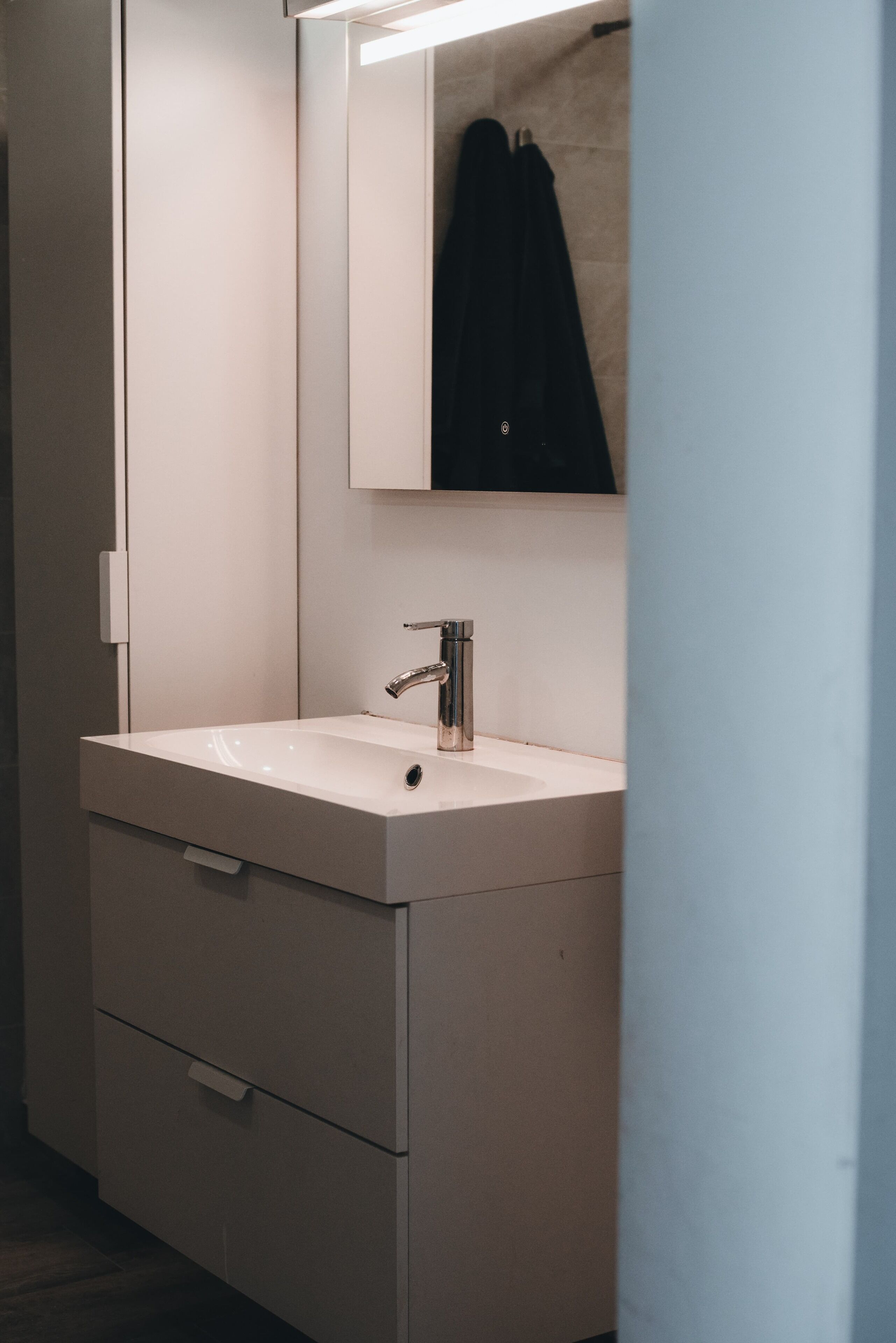 Ein modernes Badezimmer mit einem weißen Waschbecken, einem Spiegel und einem Handtuch an der Wand.