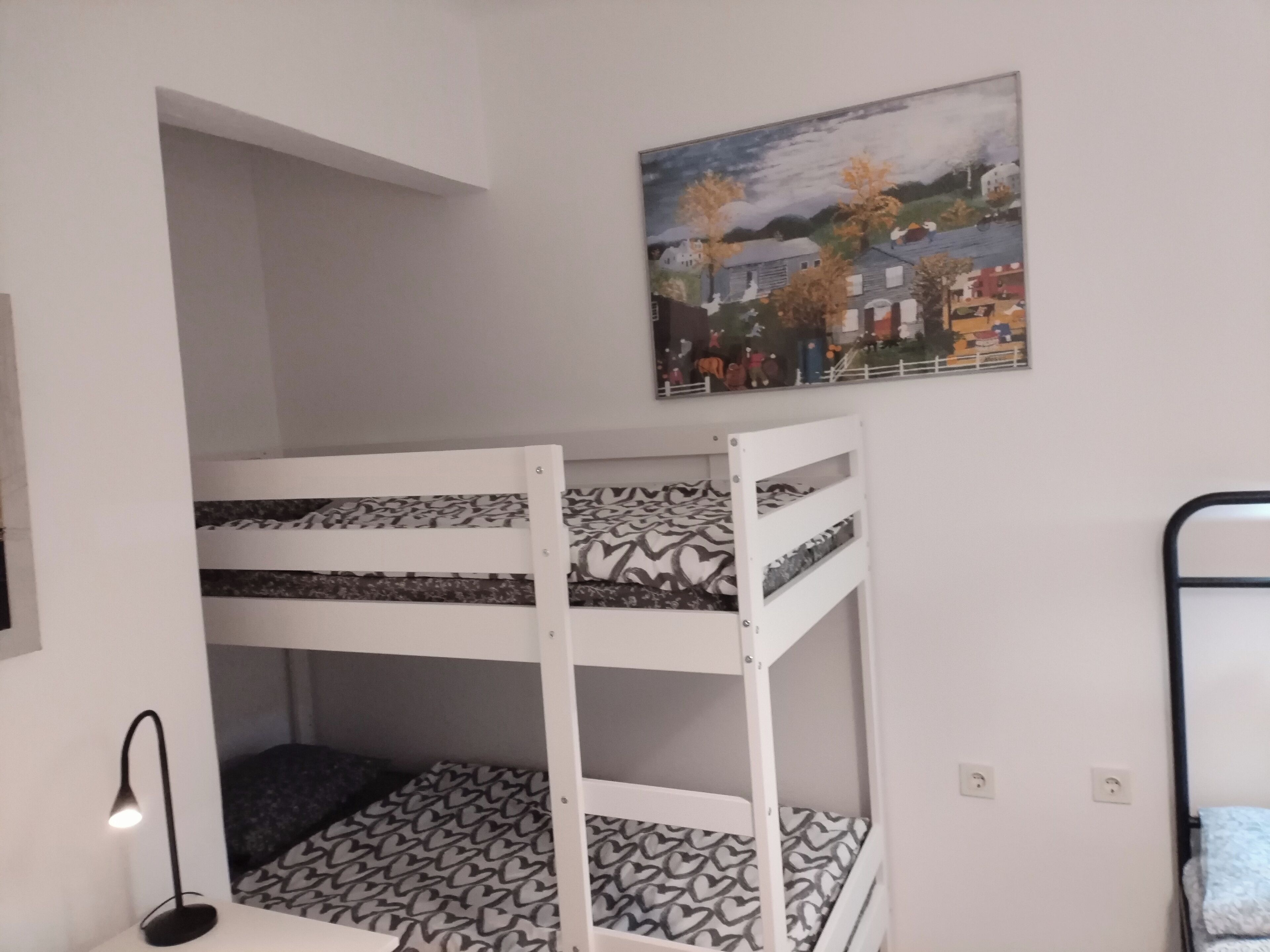Un lit superposé avec une literie à motifs, une lampe de bureau et un tableau accroché au mur.