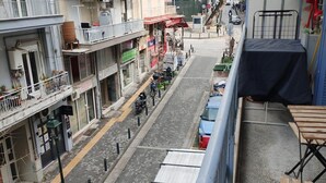 Una calle estrecha flanqueada por edificios, con un coche azul aparcado a la derecha y una motocicleta a la izquierda.