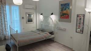 Un dormitorio con cama, ventilador de techo, equipo de aire acondicionado, ventana con cortinas y un cuadro en la pared.