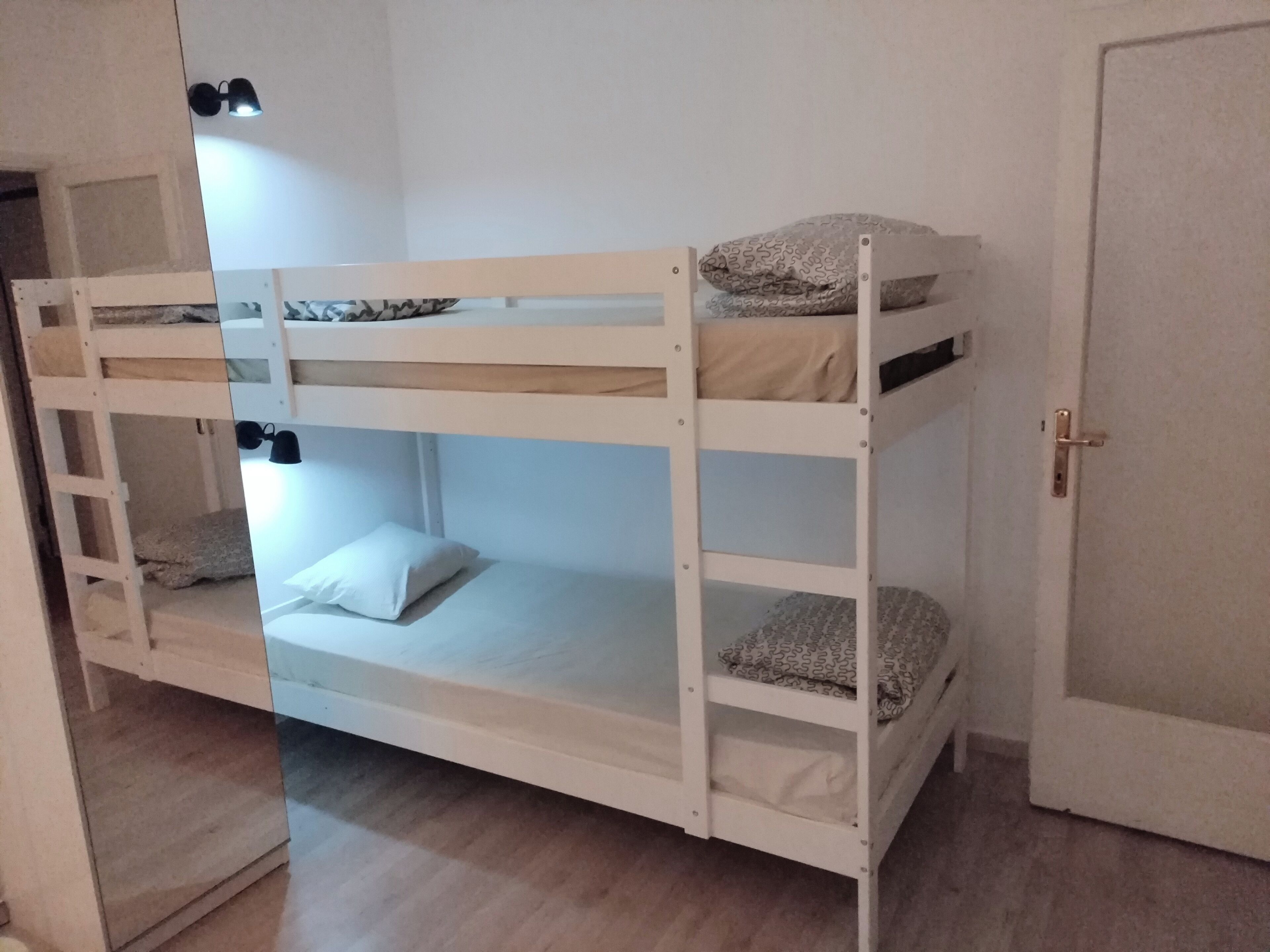 En køjeseng med stige, et natbord og en lampe fastgjort til væggen.