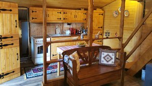A wooden cabin interior with a kitchen area, a dining table with chairs, and a staircase. - Casuta cu Brazi (Seusa)