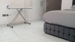 A bedroom with a bed, a wardrobe, and an ironing board. - Elite Arlington Court Apartment - East Legon (East Legon, Accra)
