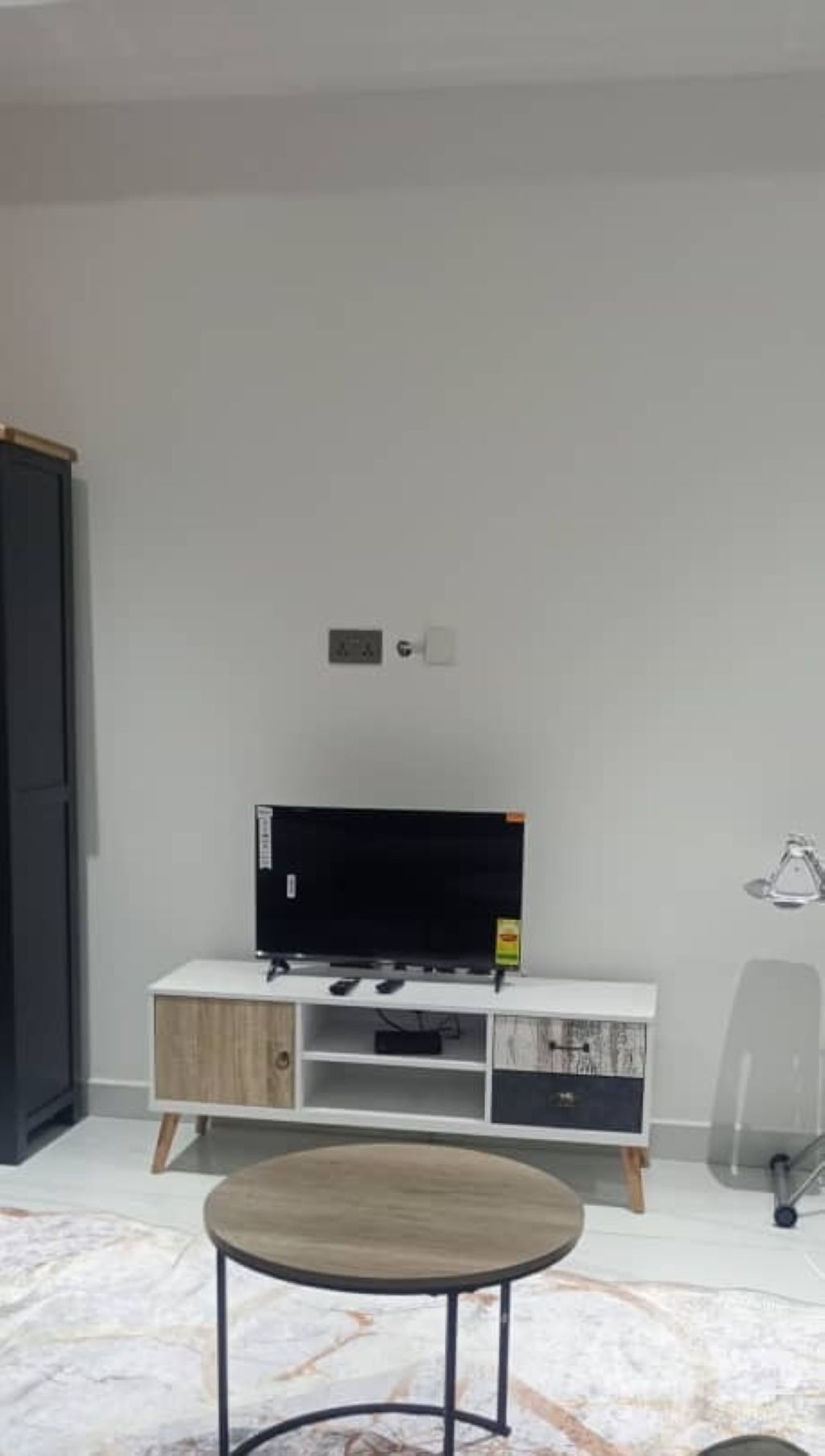 A room with a white TV stand, a flat-screen TV, a small table, and a cabinet.