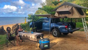 Ein Campingplatz mit Zelt, einem blauen Pick-up und einem Tisch mit Getränken und Snacks.