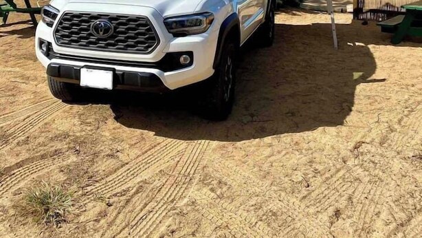 Una camioneta pickup blanca estacionada en una playa arenosa con una tienda de campaña al fondo.