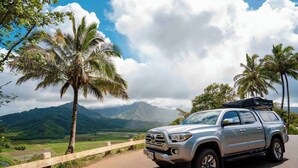 A silver SUV parked on a road with a scenic view of mountains and palm trees. - Silver Fox Camper 2018 Tacoma (Anahola)