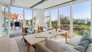 A spacious room with a large table, comfortable seating, and large windows offering a view of the outdoors. - Holiday home in Årsdale with sea view (Svaneke)